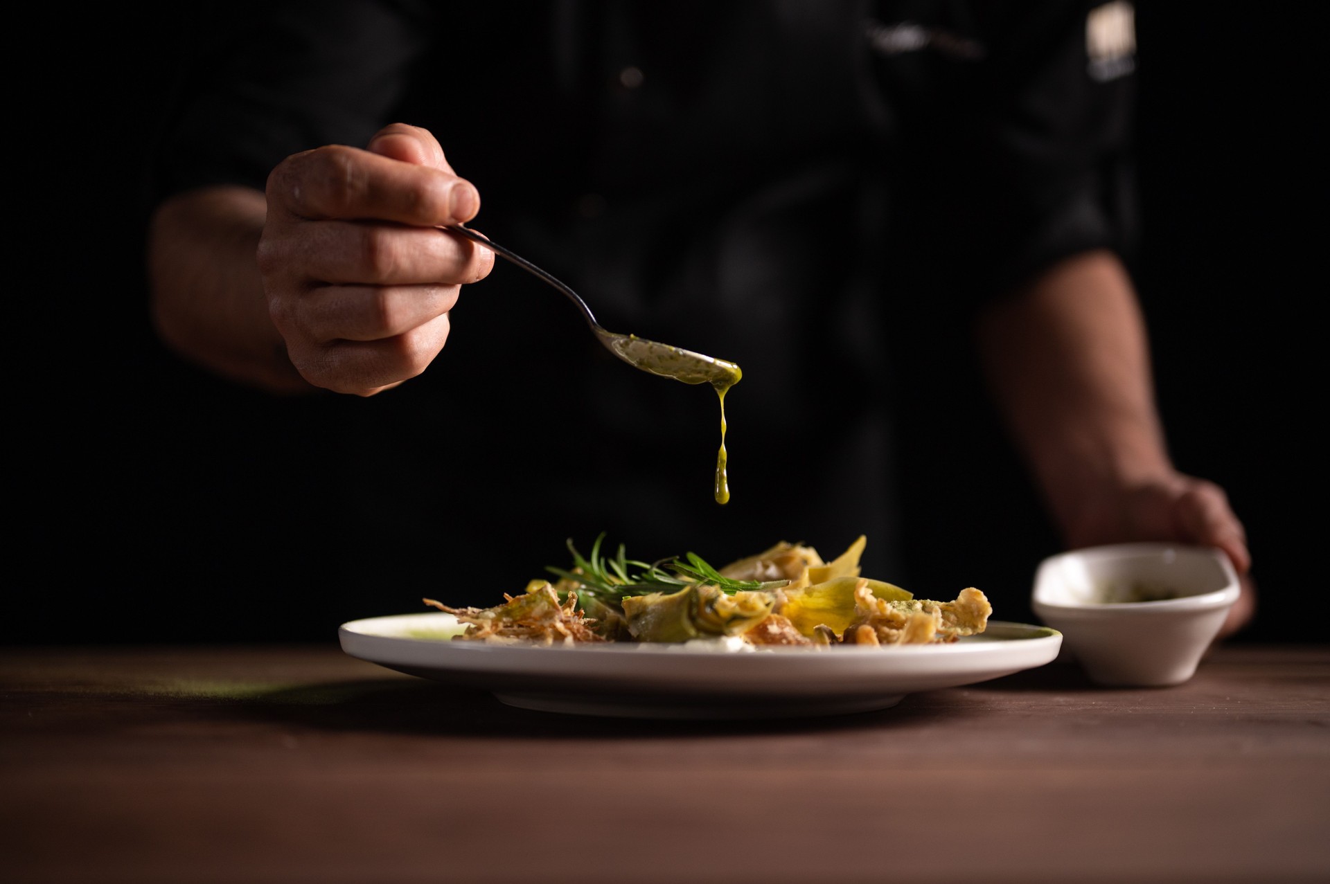 A male chef pouring sauce on on a plate of artichoke